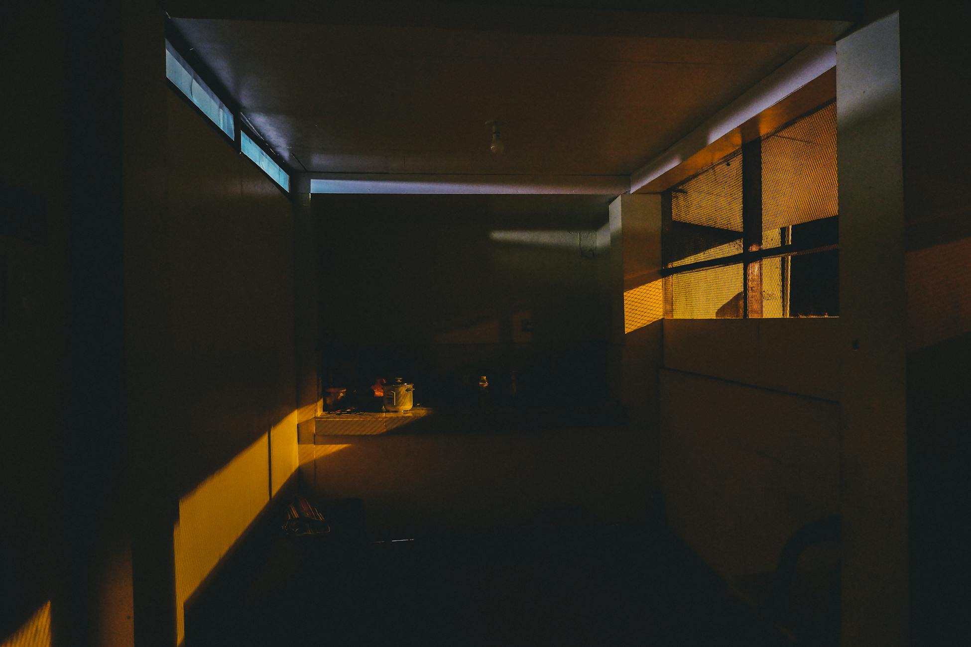 Dimly lit kitchen interior with dramatic lighting casting shadows, creating a moody atmosphere.