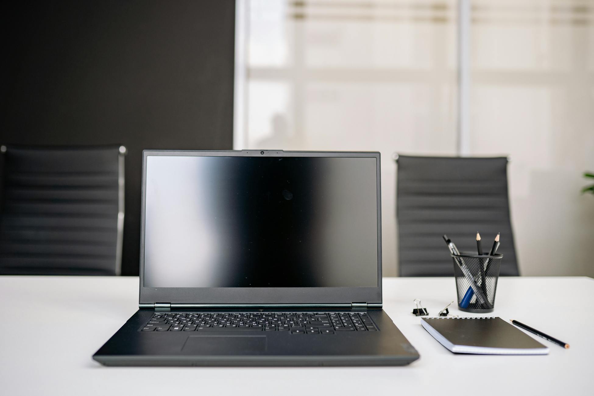 A sleek office setup featuring a laptop, notebooks, and chairs on a white desk.