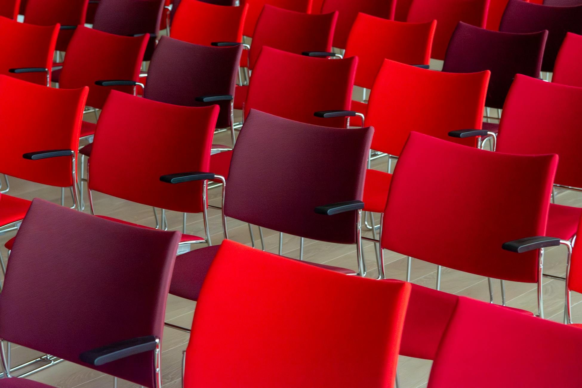 Colorful rows of empty red and burgundy chairs in an auditorium setting.