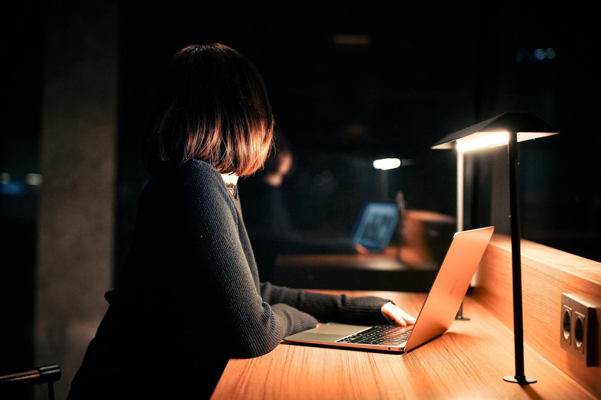 A woman works on her laptop under warm lighting, creating a calm nighttime atmosphere.