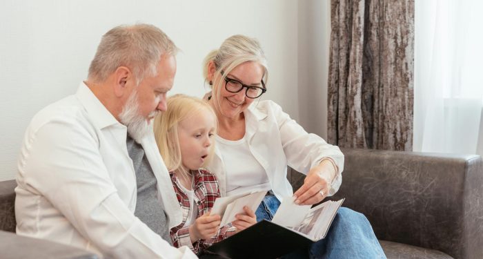 Grandparents and granddaughter cherish family memories while looking through a photo album together at home.
