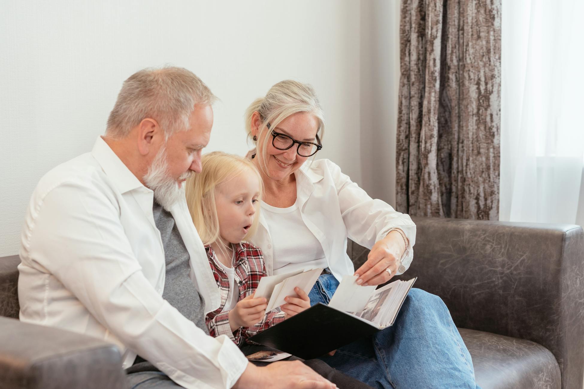 Grandparents and granddaughter cherish family memories while looking through a photo album together at home.