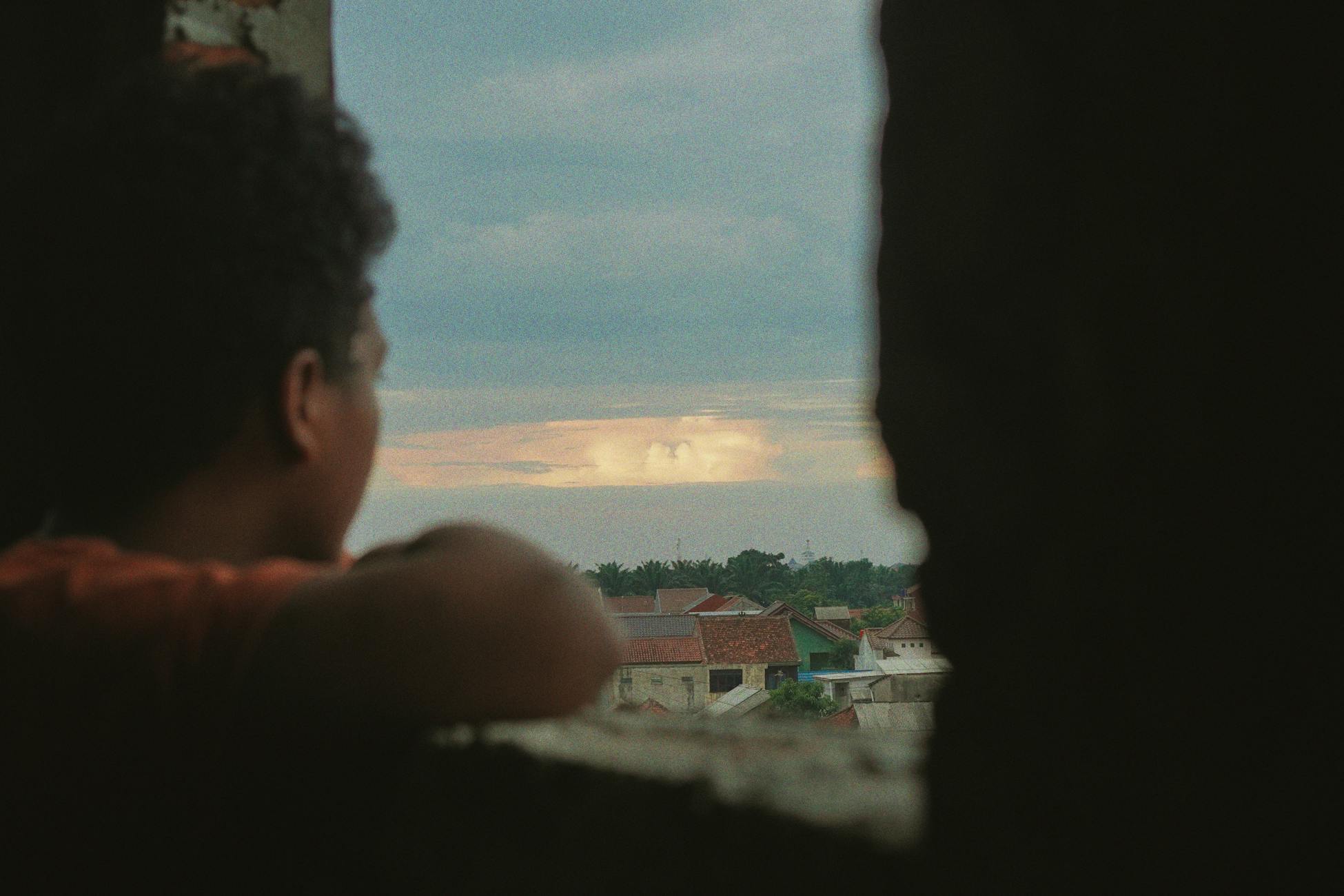 A person looks thoughtfully at the scenery through a window at sunset.