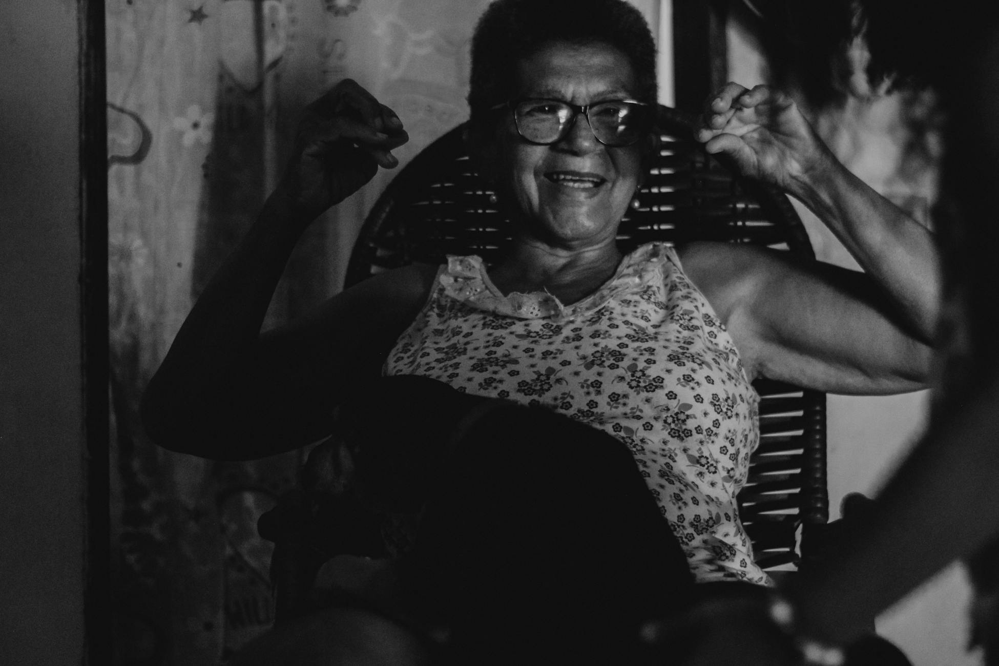 A joyful senior woman with eyeglasses enjoys a relaxed moment indoors, captured in monochrome.