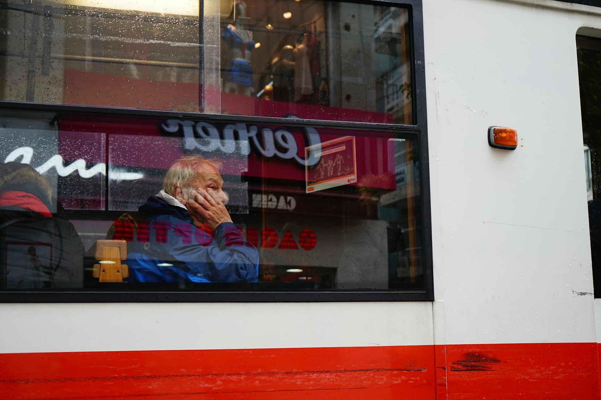 An elderly man gazes thoughtfully out a tram window, capturing a moment of reflection while traveling.