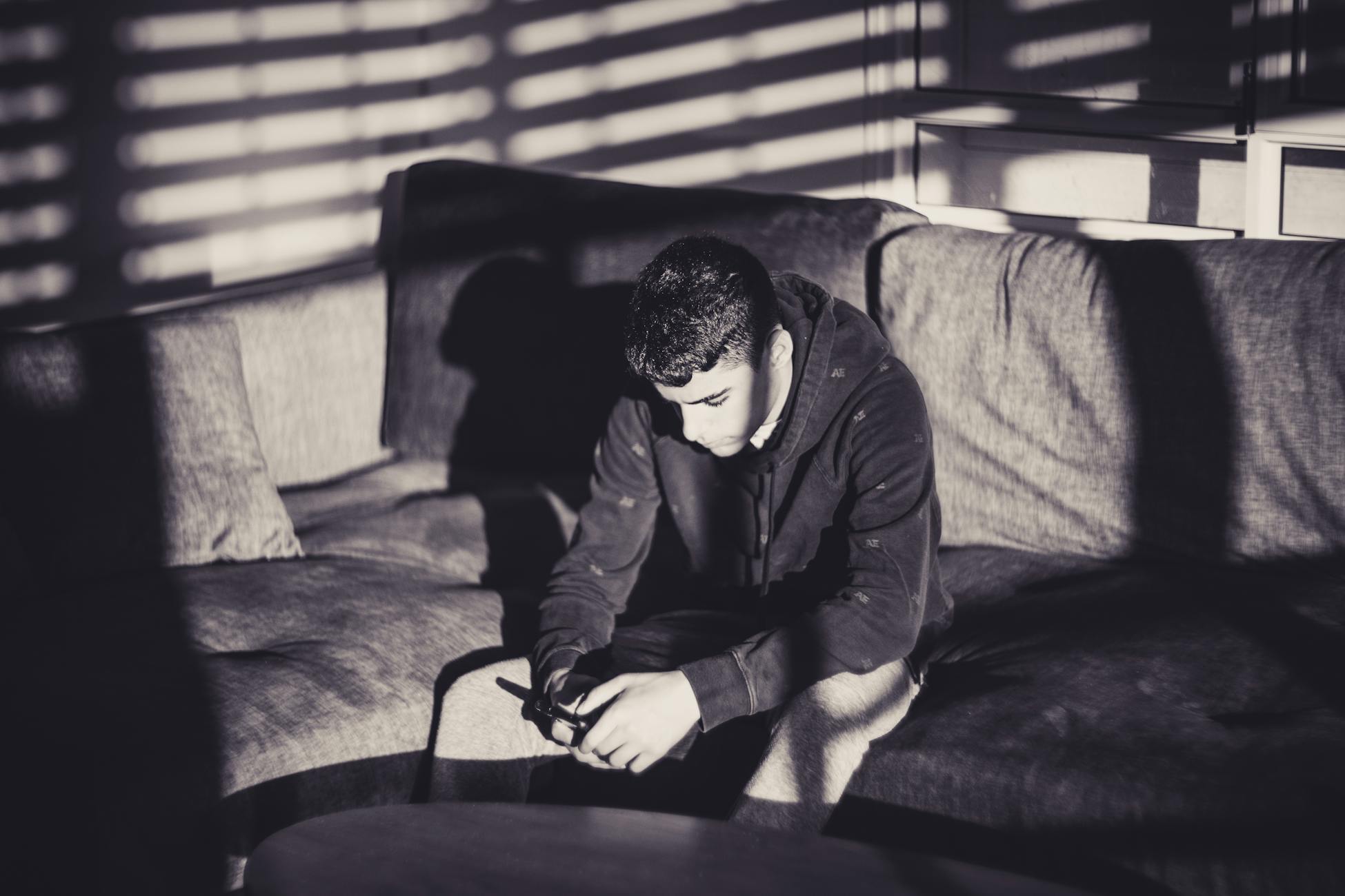 A thoughtful man looking at his phone on a sofa, captured in a dramatic black and white style.