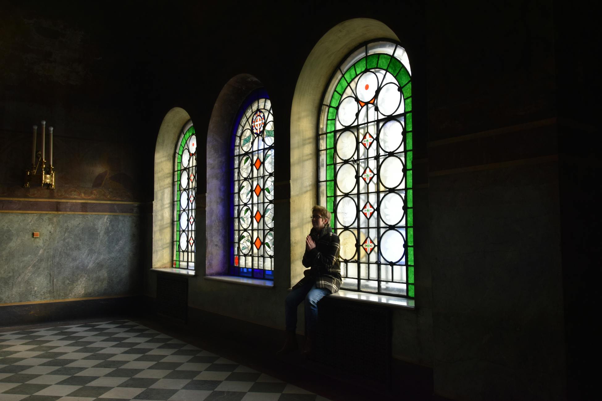 A person praying by stained glass windows, capturing a serene church atmosphere.