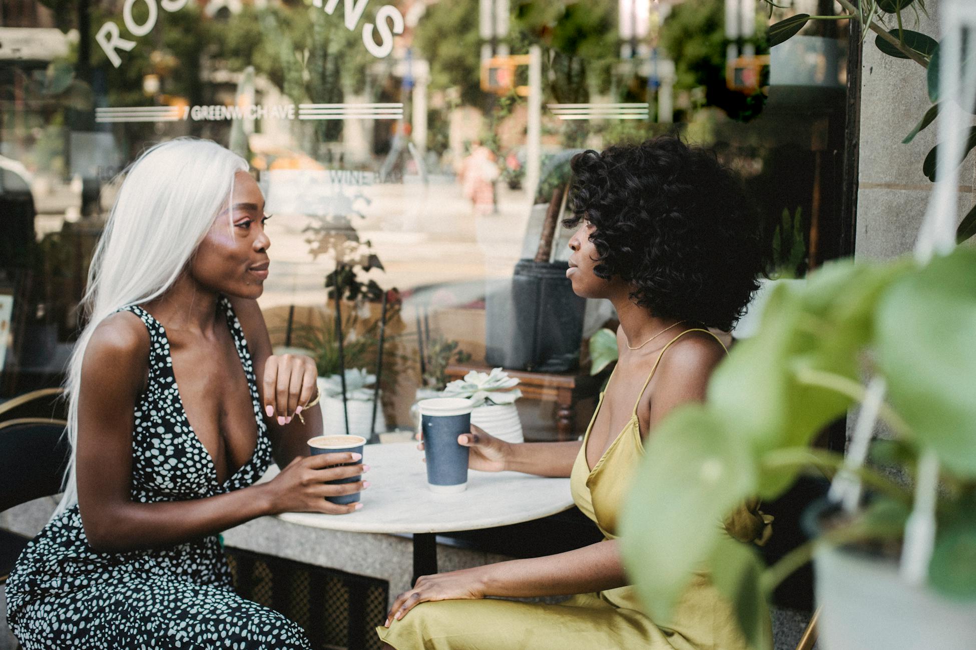 Two women enjoying coffee and conversation at an outdoor café table during the day.