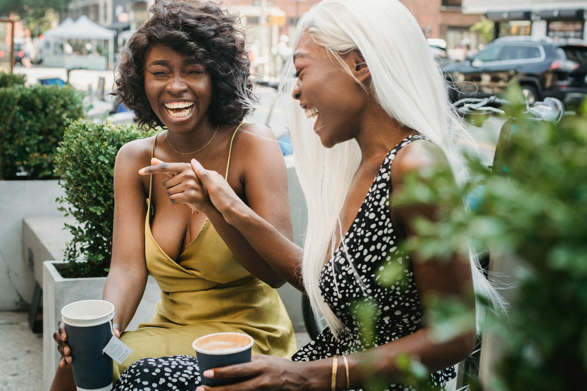 Two friends laughing together while enjoying hot drinks outside, embodying joy and companionship.