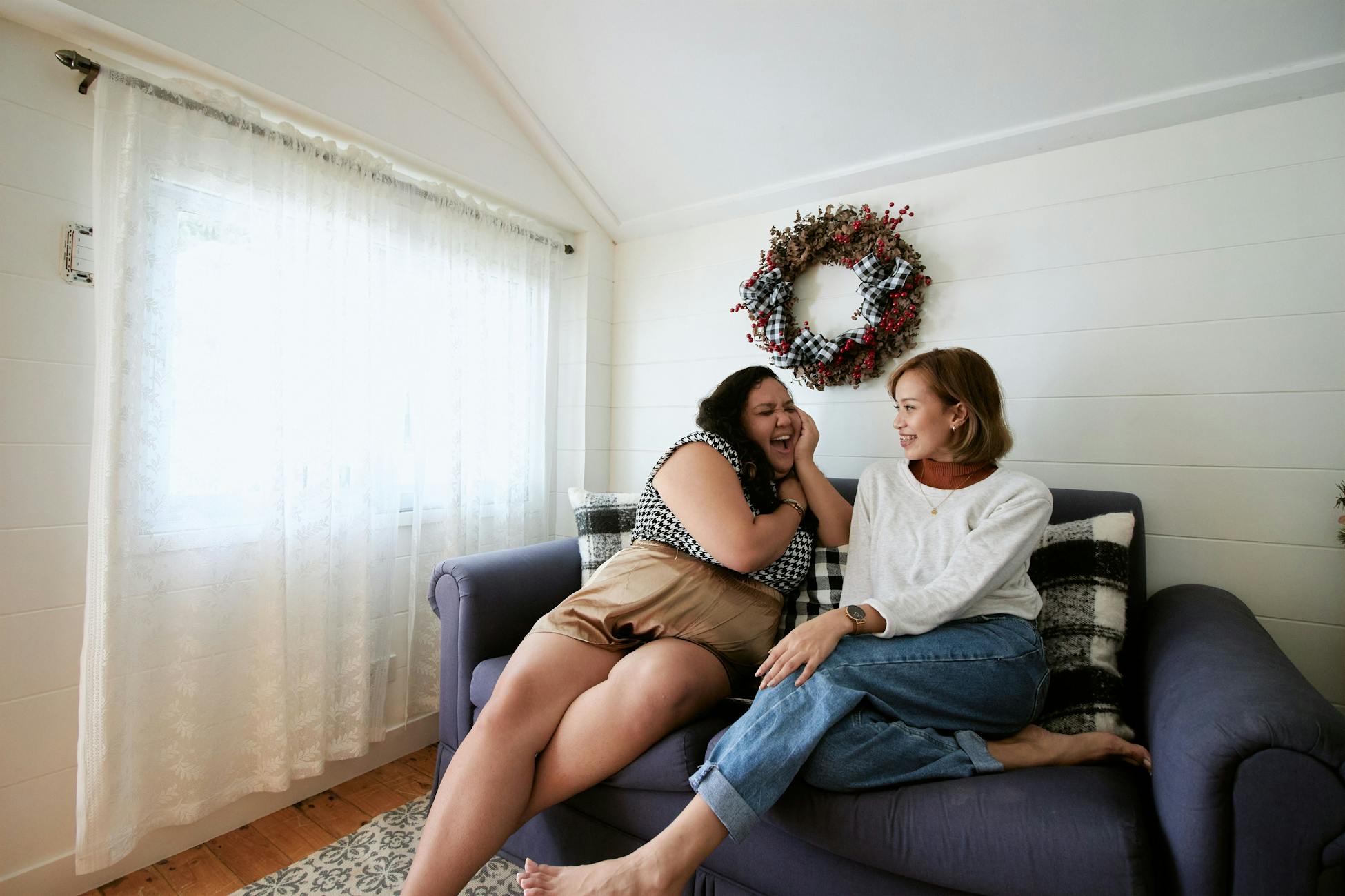 Two women enjoying a friendly conversation on a sofa in a cozy, bright living room.
