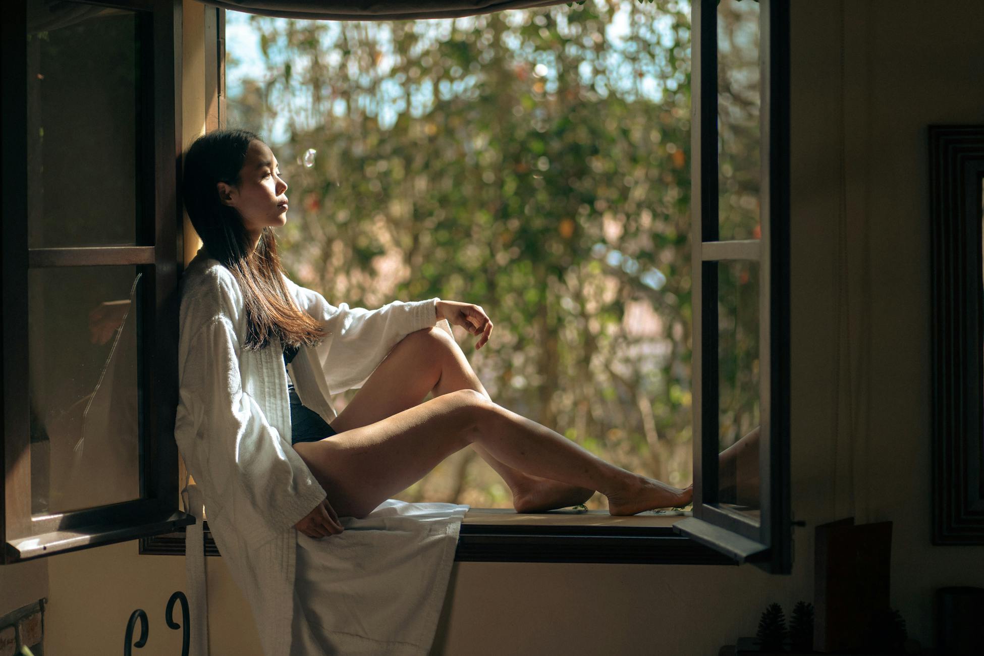 A serene moment of a woman in a bathrobe sitting in a window frame with natural light flowing in, captured in Dalat, Vietnam.
