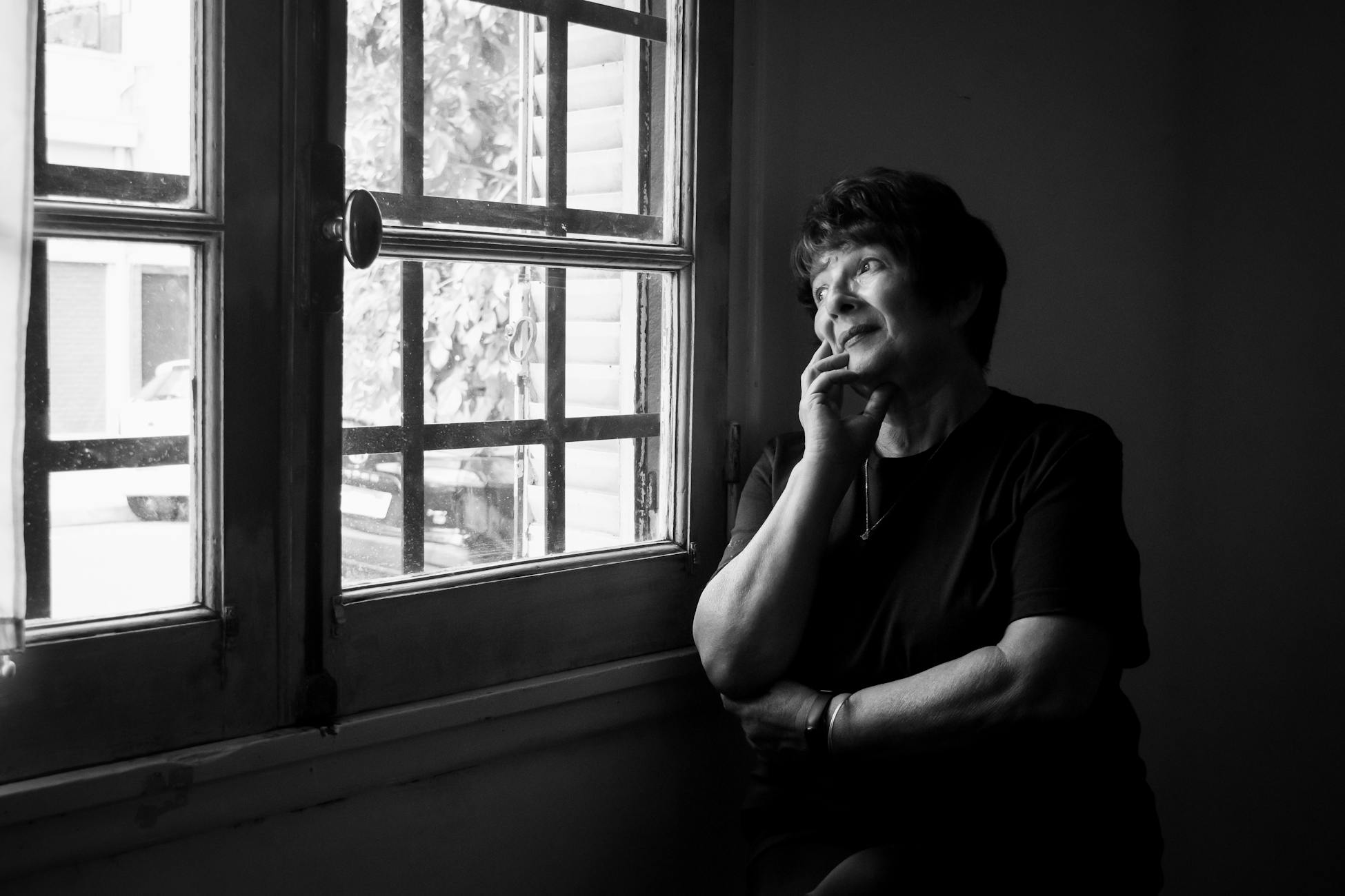Black and white portrait of a thoughtful elderly woman gazing out a window.
