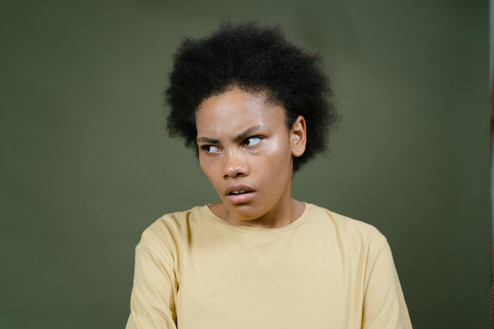 Close-up of a young woman with afro expressing a pensive mood against a green background.