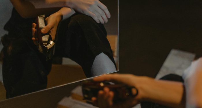 A person is reflected in the mirror holding an electric shaver indoors.