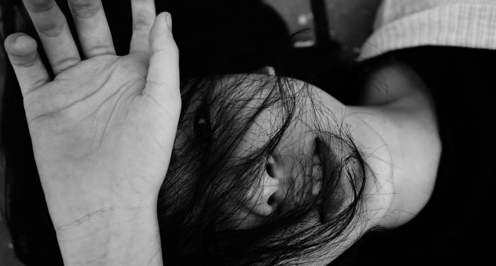 Black and white top view of anonymous emotionless young lady lying on surface with dark hair and hand on face in daytime