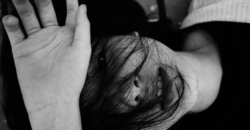 Black and white top view of anonymous emotionless young lady lying on surface with dark hair and hand on face in daytime