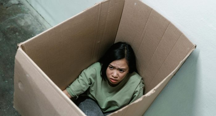 Woman in a cardboard box, symbolizing feelings of anxiety and claustrophobia.
