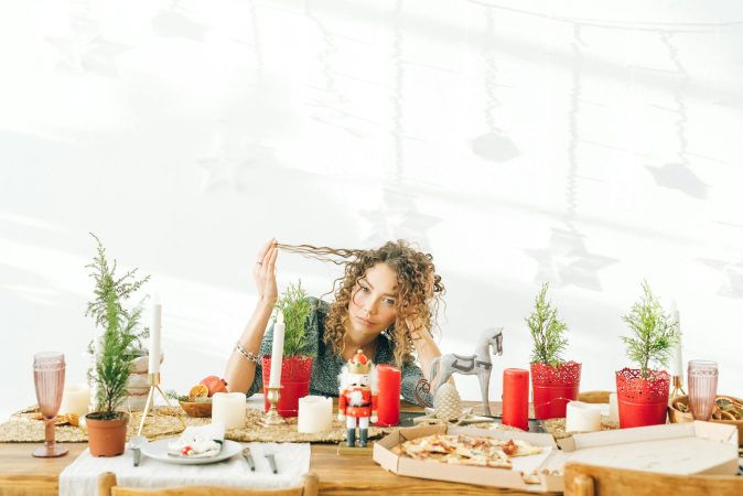 A woman with curly hair sits at a decorated dining table with candles and potted plants.
