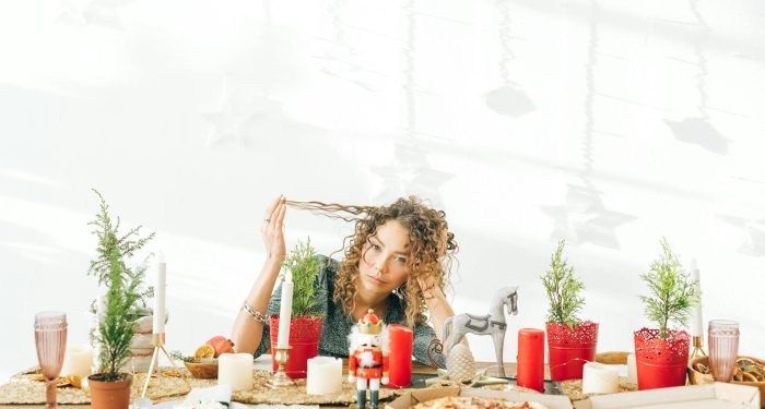 A woman with curly hair sits at a decorated dining table with candles and potted plants.