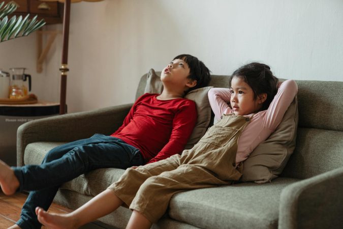 Two children lounging on a sofa in a living room, enjoying leisure time indoors.