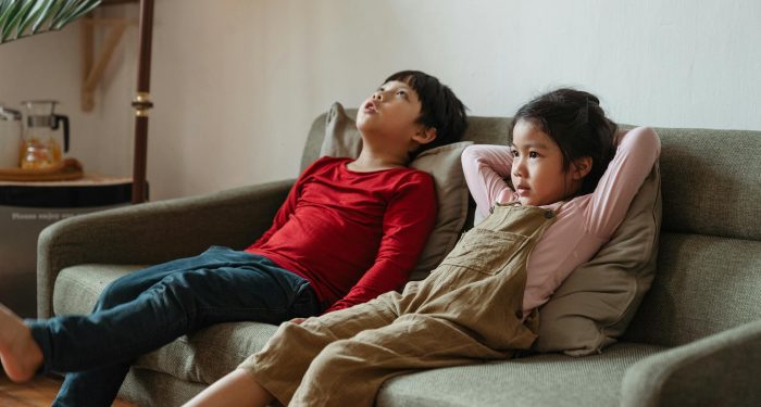 Two children lounging on a sofa in a living room, enjoying leisure time indoors.