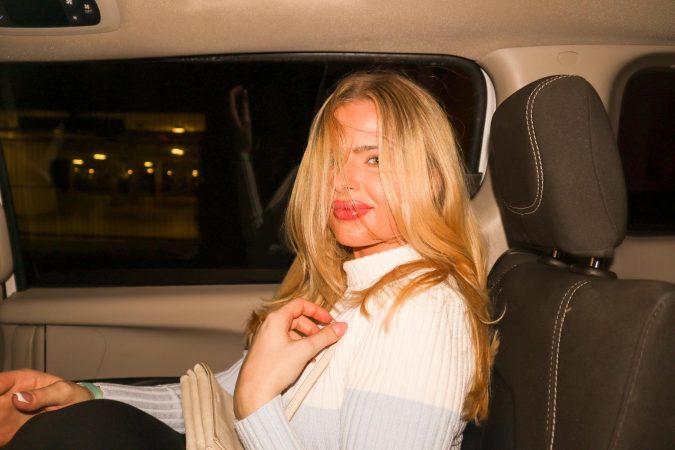 A young woman with blonde hair sitting in the backseat of a car at night.