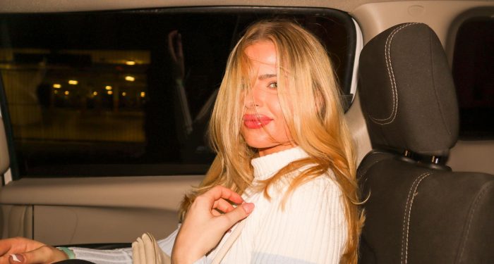 A young woman with blonde hair sitting in the backseat of a car at night.