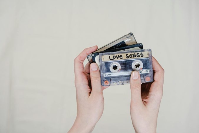 Close-up of hands holding retro cassette tapes labeled 'Love Songs' on a light background.