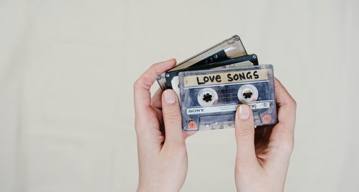 Close-up of hands holding retro cassette tapes labeled 'Love Songs' on a light background.