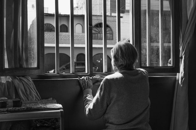 A senior woman looks out a window, symbolizing solitude and contemplation.