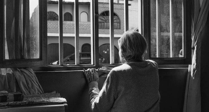 A senior woman looks out a window, symbolizing solitude and contemplation.
