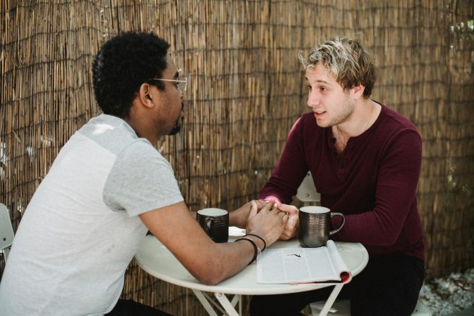 Interracial gay couple holding hands and enjoying coffee together at an outdoor cafe.