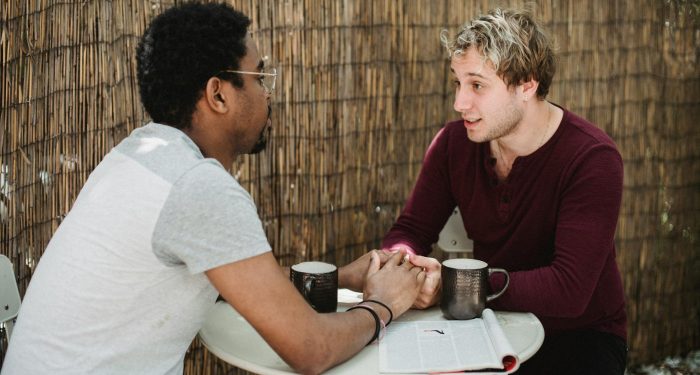 Interracial gay couple holding hands and enjoying coffee together at an outdoor cafe.