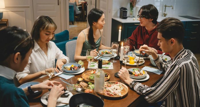 A diverse group of friends sharing dinner at a cozy dining table with wine and lighted candles.