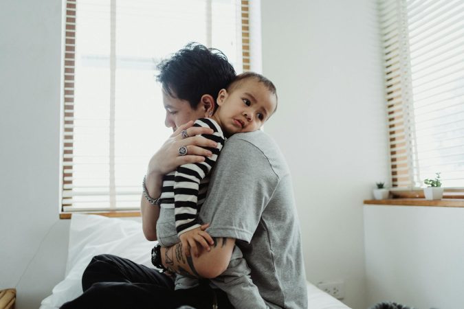 A heartfelt embrace between a parent with short hair and a child on a bed, creating a warm family scene.