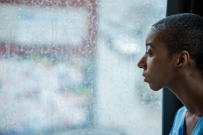 Side view of crop African American woman with short dark hair sitting near wet window in rainy day and looking away