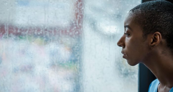 Side view of crop African American woman with short dark hair sitting near wet window in rainy day and looking away
