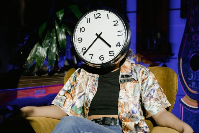 A surreal image of a person sitting in an armchair with a clock as a face, evoking themes of time and identity.