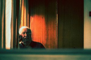 Elderly man staring contemplatively through window, captured in a moody vintage style.