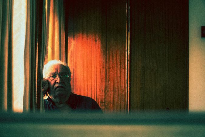 Elderly man staring contemplatively through window, captured in a moody vintage style.