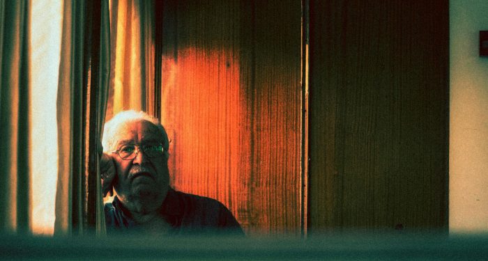 Elderly man staring contemplatively through window, captured in a moody vintage style.