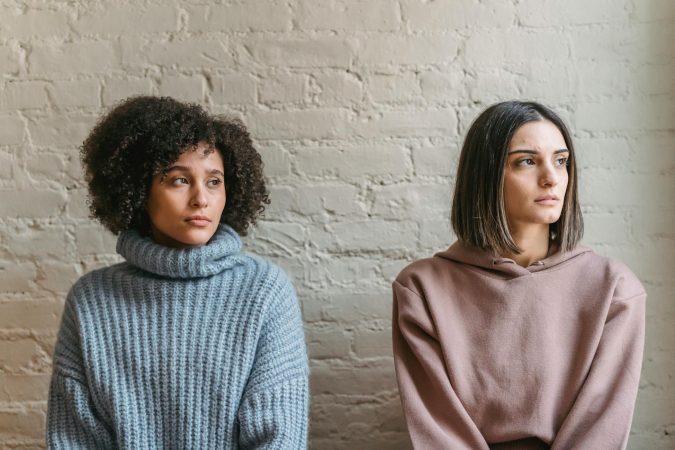 Sad African American woman with female friend in casual clothes looking away while sitting in light room during quarrel at home