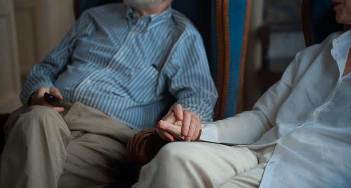An elderly couple sitting together, holding hands in a cozy room, symbolizing companionship.
