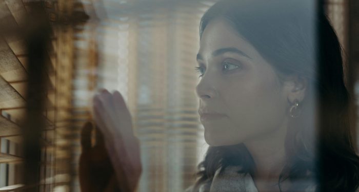 A thoughtful woman peeks through window blinds, creating a contemplative mood.