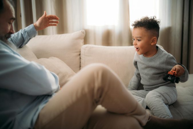 A young boy playing with a toy car with his grandfather on the couch at home.