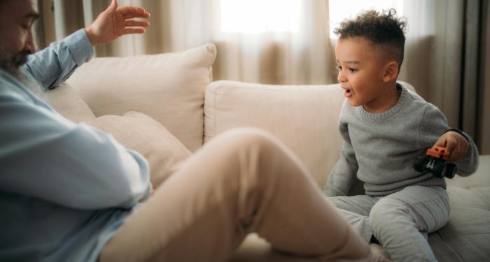 A young boy playing with a toy car with his grandfather on the couch at home.