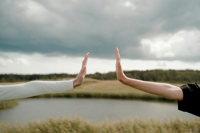 Two arms reaching out for a high five, symbolizing connection and distance in a natural setting.