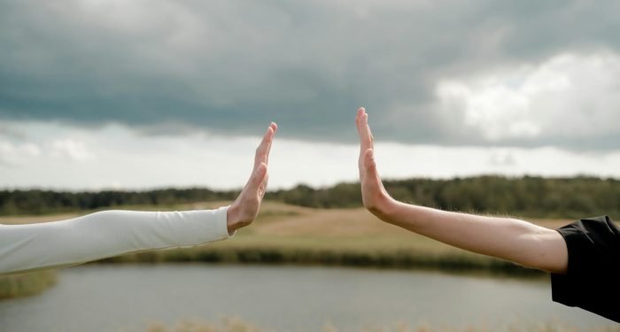 Two arms reaching out for a high five, symbolizing connection and distance in a natural setting.