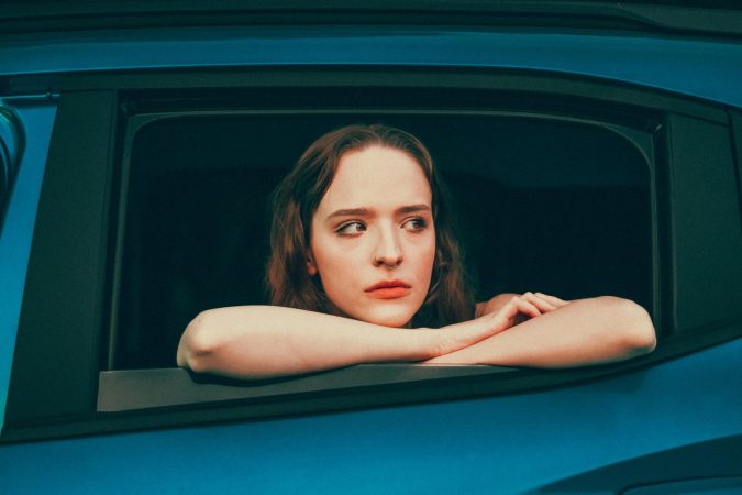 A woman leans on a car window, looking thoughtfully outside with a soft expression.