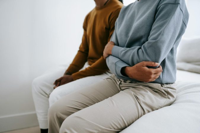 Crop faceless young black couple in casual outfit resting together in bedroom in daytime